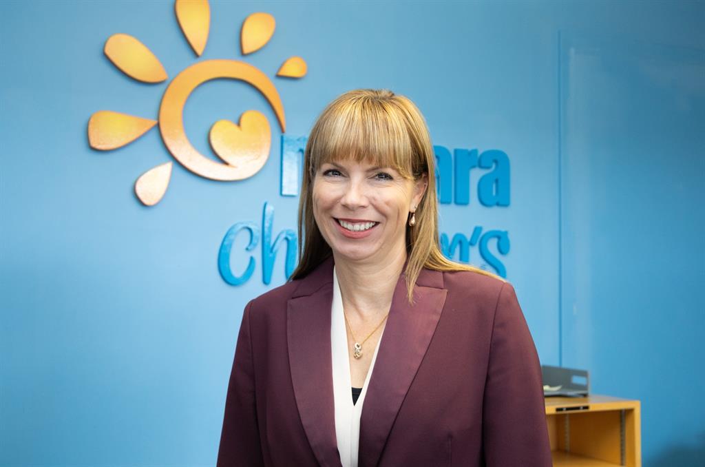 Women in purple blazer stands in front of blue background